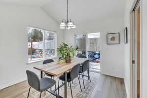 Dining room with an inviting chandelier, vaulted ceiling, and light wood-type flooring