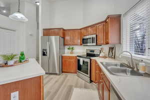 Kitchen featuring sink, light wood-type flooring, pendant lighting, stainless steel appliances, and a high ceiling