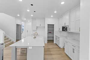 Kitchen featuring sink, white cabinetry, tasteful backsplash, a center island with sink, and light wood-type flooring