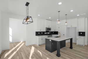 Kitchen featuring appliances with stainless steel finishes, an island with sink, sink, white cabinets, and hanging light fixtures