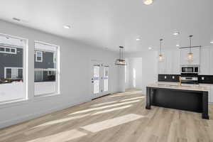 Kitchen featuring appliances with stainless steel finishes, decorative light fixtures, tasteful backsplash, white cabinets, and a kitchen island with sink