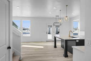 Kitchen with light hardwood / wood-style floors, decorative light fixtures, a kitchen breakfast bar, and sink