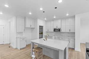 Kitchen with sink, light hardwood / wood-style floors, white cabinets, and a center island with sink