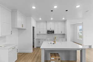 Kitchen with white cabinetry, light hardwood / wood-style floors, sink, and backsplash