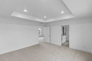 Unfurnished bedroom featuring a tray ceiling and light colored carpet