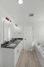 Bathroom featuring a relaxing tiled tub, wood-type flooring, and vanity