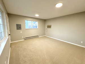 Carpeted spare room featuring a wall unit AC, electric panel, and baseboard heating