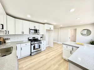 Kitchen featuring light stone counters, tasteful backsplash, stainless steel appliances, and white cabinets