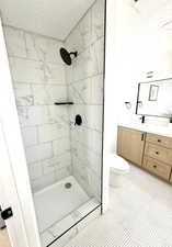 Bathroom featuring tiled shower, vanity, toilet, and a textured ceiling