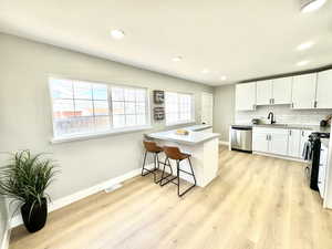 Kitchen with a breakfast bar, dishwasher, range with electric stovetop, white cabinets, and decorative backsplash