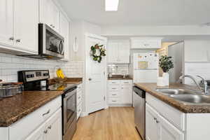 Kitchen with sink, white cabinets, decorative backsplash, stainless steel appliances, and light hardwood / wood-style flooring