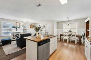 Kitchen featuring sink, white cabinetry, a center island with sink, dishwasher, and a notable chandelier