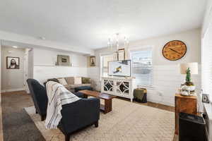 Living room featuring an inviting chandelier, wooden walls, light colored carpet, and a textured ceiling