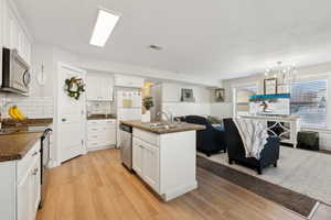 Kitchen featuring pendant lighting, sink, white cabinets, stainless steel appliances, and a center island with sink