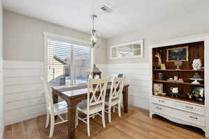 Dining area with light hardwood / wood-style floors, a chandelier, and wood walls