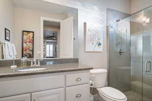 Bathroom featuring walk in shower, ceiling fan, vanity, and toilet