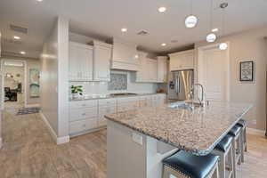 Kitchen featuring sink, a center island with sink, custom exhaust hood, and appliances with stainless steel finishes