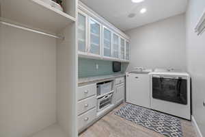 Clothes washing area with light hardwood / wood-style flooring, washing machine and dryer, and cabinets