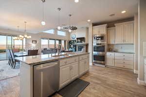 Kitchen with sink, light stone counters, hanging light fixtures, an island with sink, and stainless steel appliances