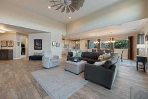 Living room featuring a towering ceiling, ceiling fan with notable chandelier, and light wood-type flooring