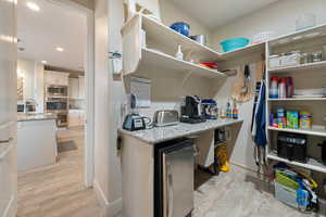 Interior space with appliances with stainless steel finishes, decorative light fixtures, wine cooler, light hardwood / wood-style floors, and light stone countertops