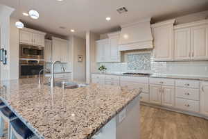 Kitchen featuring sink, light stone counters, decorative light fixtures, custom range hood, and stainless steel appliances