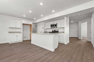 Kitchen featuring sink, dark wood-type flooring, stainless steel appliances, white cabinets, and a center island with sink