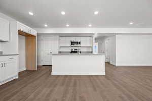 Kitchen with stainless steel appliances, a kitchen island with sink, hardwood / wood-style floors, and white cabinets