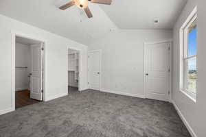 Unfurnished bedroom featuring dark colored carpet, lofted ceiling, a spacious closet, and ceiling fan