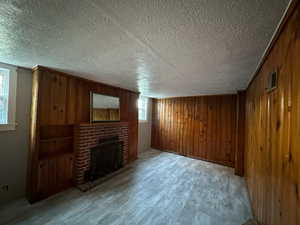 Unfurnished living room with light hardwood / wood-style flooring, a brick fireplace, wooden walls, and a textured ceiling