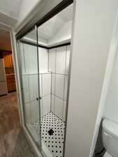 Bathroom featuring laminate flooring, an enclosed tile shower, a textured ceiling, and toilet