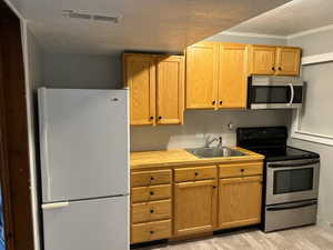 Kitchen with appliances with stainless steel finishes, sink, a textured ceiling, and laminate flooring.