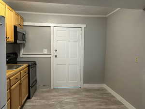 Kitchen featuring stainless steel appliances, crown molding, a textured ceiling, and light wood-type flooring