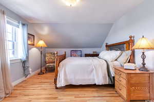 Spacious upstairs Bedroom with vaulted ceiling and light hardwood flooring