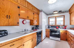 Kitchen with black dishwasher, sink, a textured ceiling, and gas range / gas stove