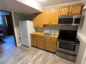 Kitchen with sink, crown molding, a textured ceiling, laminate flooring, and appliances with stainless steel finishes