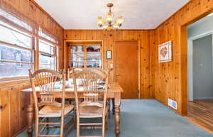 Carpeted dining room with an inviting chandelier and wood walls