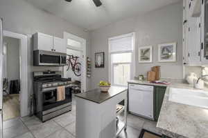 Kitchen with appliances with stainless steel finishes, sink, white cabinets, light tile patterned floors, and ceiling fan