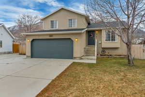 Split level home featuring a mountain view, a garage, and a front lawn