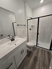 Bathroom featuring vanity, toilet, a shower with shower door, and hardwood / wood-style floors