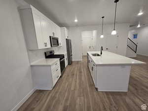 Kitchen with appliances with stainless steel finishes, decorative light fixtures, sink, white cabinets, and a center island with sink