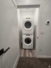 Clothes washing area with dark hardwood / wood-style floors and stacked washer / dryer