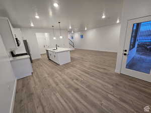 Kitchen featuring pendant lighting, sink, light hardwood / wood-style floors, white cabinets, and a center island with sink