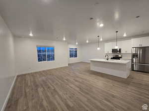 Kitchen with pendant lighting, white cabinetry, stainless steel appliances, and a center island with sink