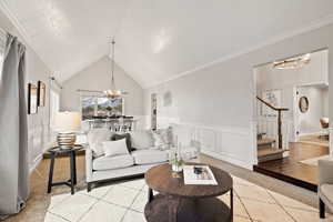 Living room with crown molding, vaulted ceiling, light colored carpet, and an inviting chandelier