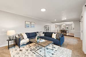 Living room with crown molding, light carpet, and a notable chandelier