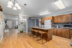 Kitchen with pendant lighting, a breakfast bar area, a center island, white refrigerator, and light wood-type flooring