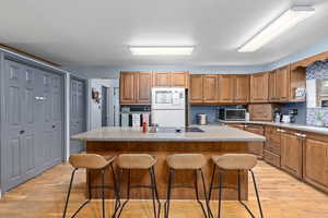 Kitchen with a kitchen island, sink, a kitchen breakfast bar, black appliances, and light hardwood / wood-style flooring