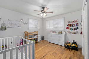 Bedroom with a crib, ceiling fan, and light hardwood / wood-style floors