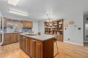 Kitchen featuring light wood-type flooring, a kitchen breakfast bar, hanging light fixtures, a center island, and black electric cooktop